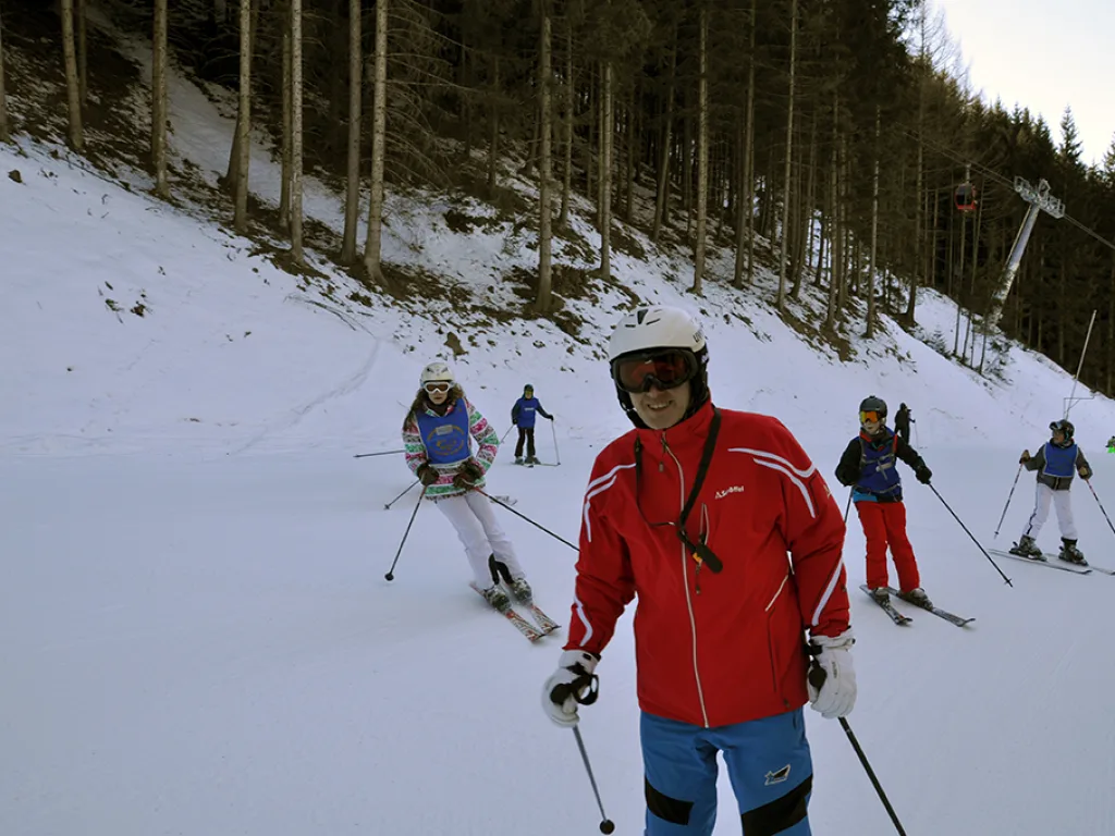 Skifahrer in roter Jacke auf der Piste am Waldrand.